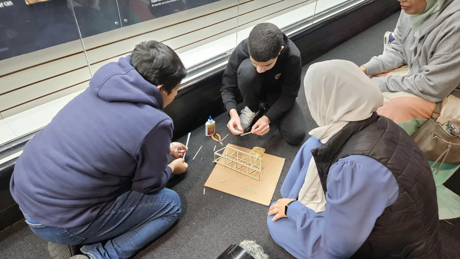 four students kneel together while assembling a bridge on the floor